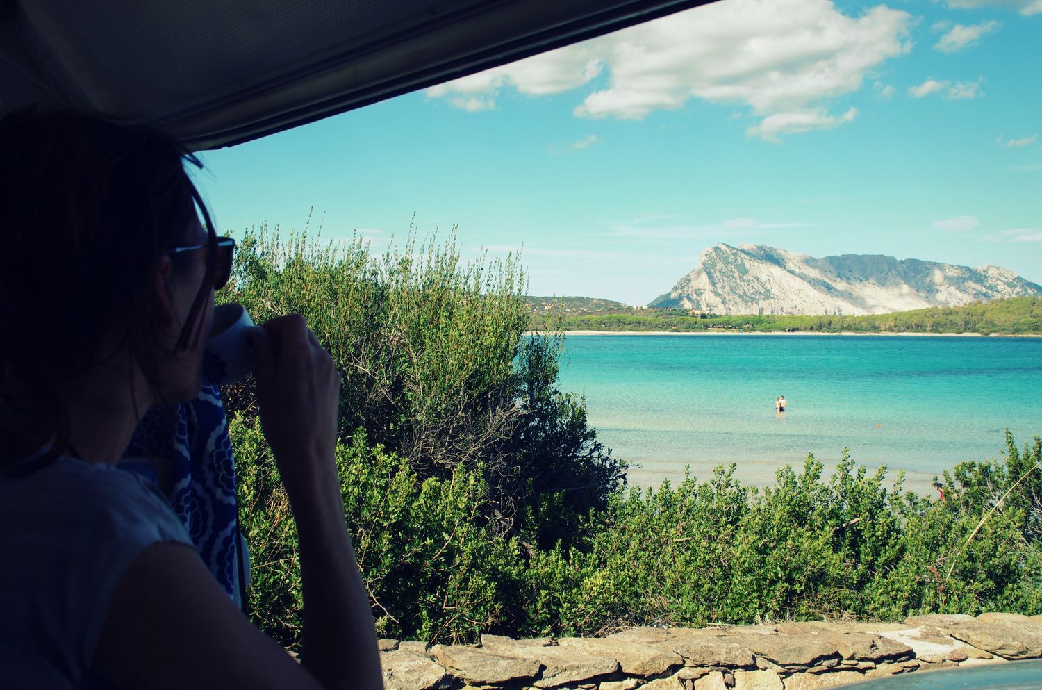 fille buvant un café face à plage aux eaux turquoises