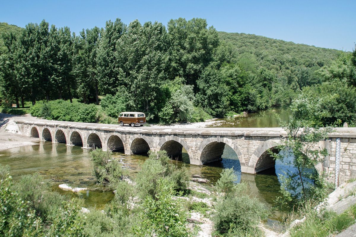 Marcel, le combi vw marron de Les vieilles qui roulent qui passe sur le pont de pierre de Montclus